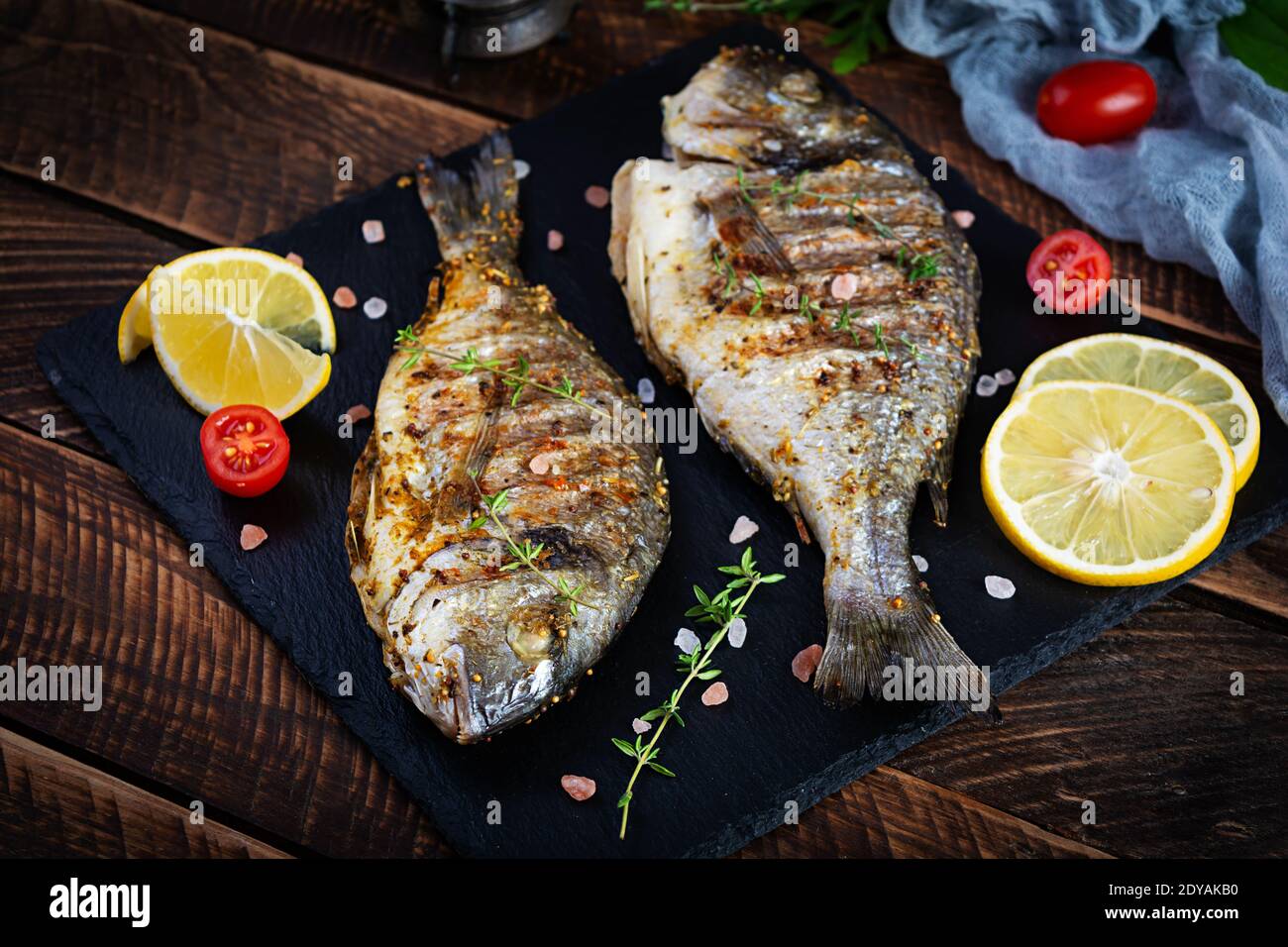 Pesce dorado alla griglia su sfondo di legno. Pesce arrosto con spezie ed erbe Foto Stock