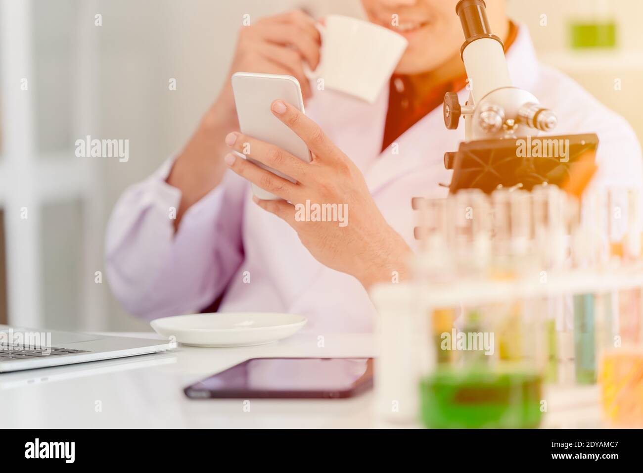 Medico scienziato con caffè del mattino e controllare le buone notizie da lo smartphone in laboratorio si sente felice e sorridente Foto Stock