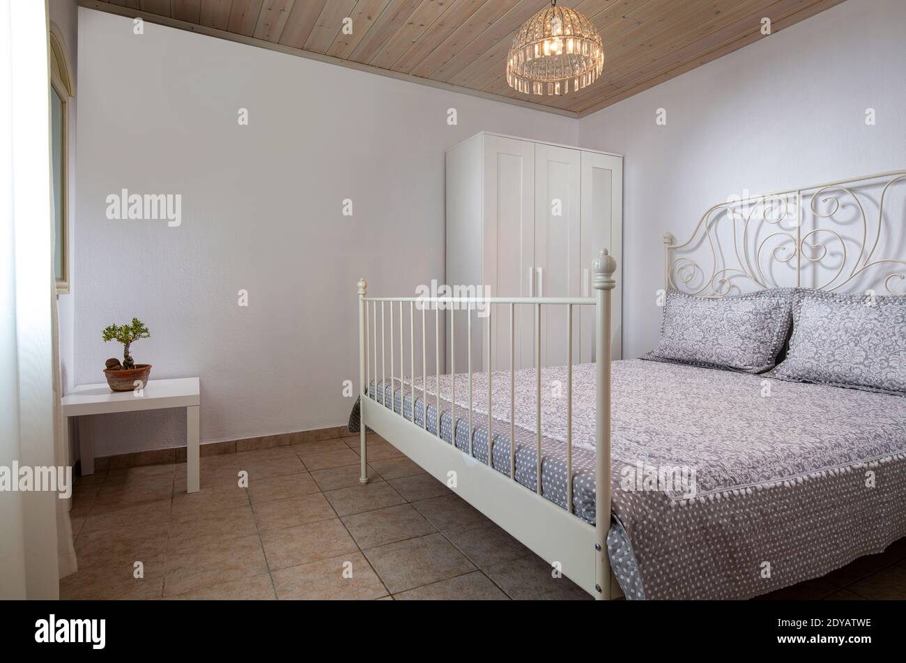 Interni in stile classico con camera da letto bianca con letto forgiato, soffitto in legno, pavimento in piastrelle di ceramica su sfondo vuoto spazio copia parete Foto Stock