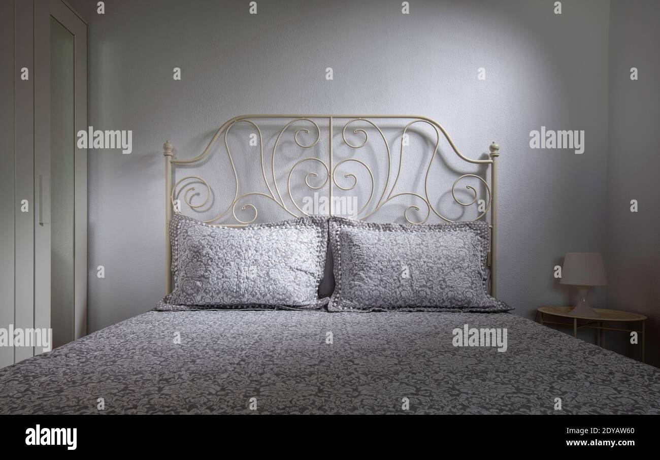 Vista frontale della camera da letto interna in stile classico con letto matrimoniale, testiera forgiata, biancheria da letto in pizzo su sfondo bianco Foto Stock