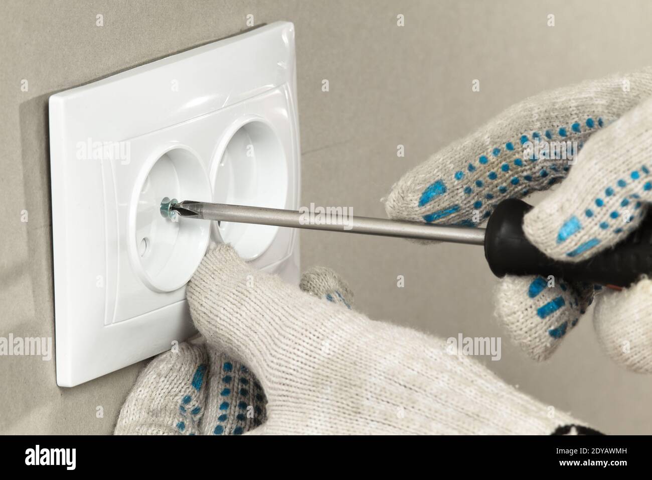 le mani dell'elettricista con un cacciavite serrano la vite che fissa la presa elettrica, chiudere Foto Stock