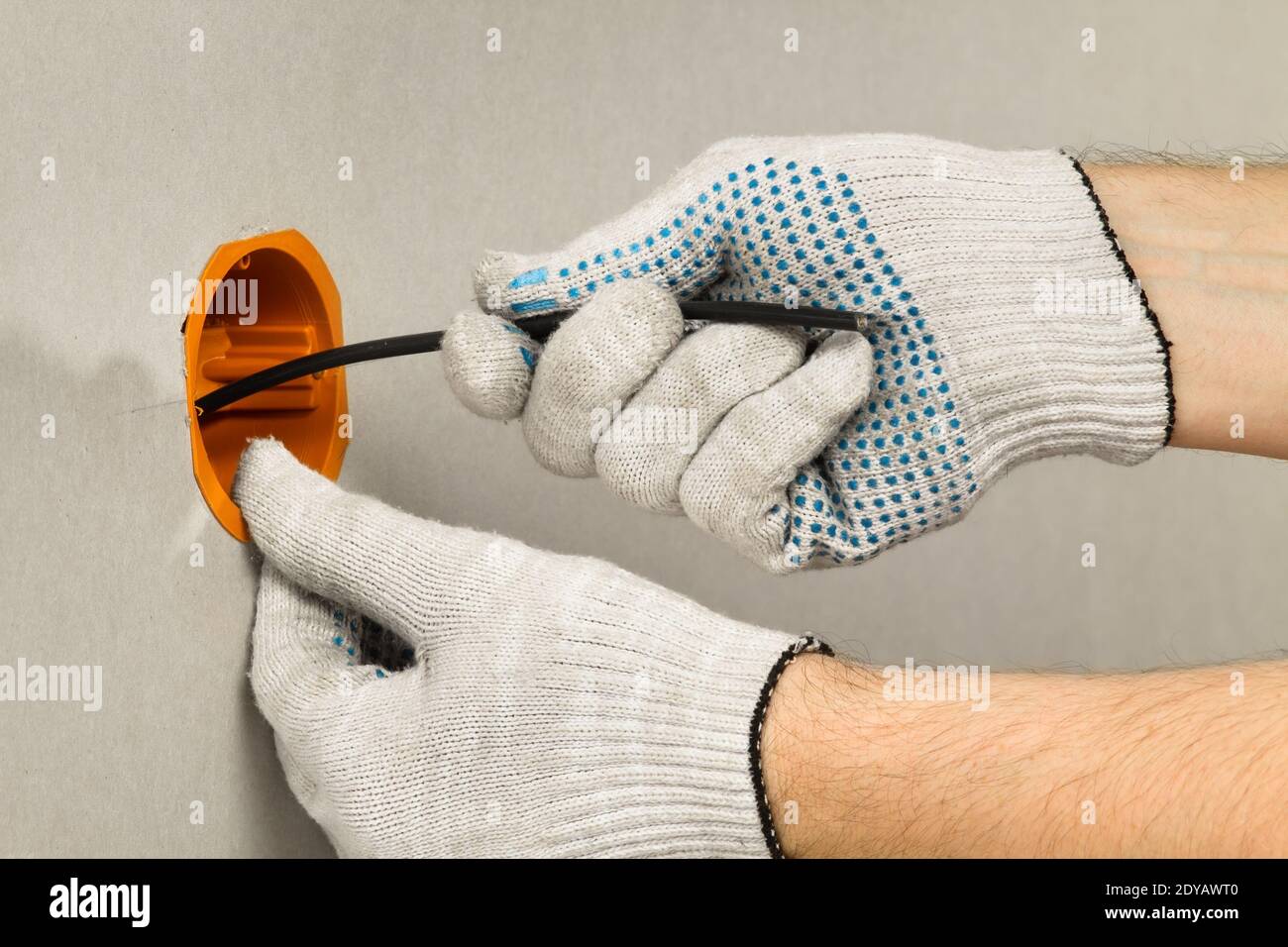 la mano di un elettricista in un guanto conduce il cavo nelle prese della scatola sulla parete di cartongesso, closeup Foto Stock