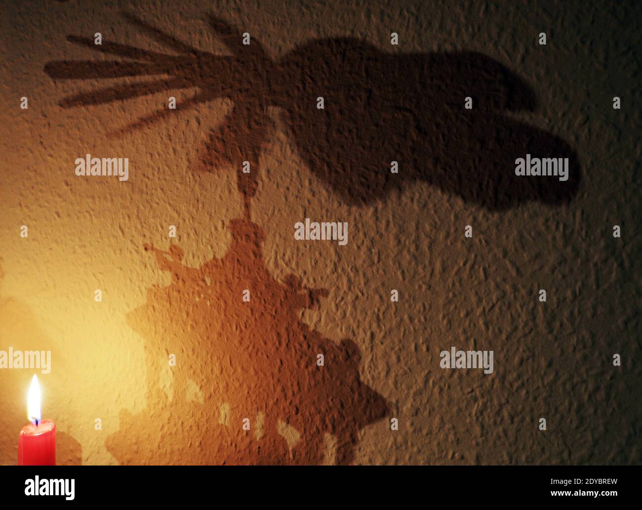 Weimar, Germania. 23 dicembre 2020. L'ombra di una piramide di Natale accanto alla fiamma di una candela rossa bruciante sulla parete coperta con carta da parati Ingrain crea un'atmosfera di Natale. Credit: Soeren Stache/dpa-Zentralbild/ZB/dpa/Alamy Live News Foto Stock