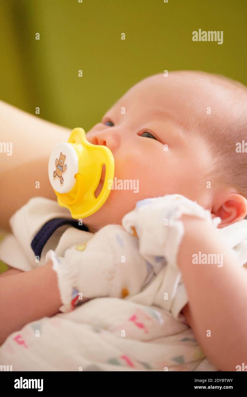 Neonato bambina cinese di meno di un mese succhiando felicemente sul suo succhietto. Foto Stock