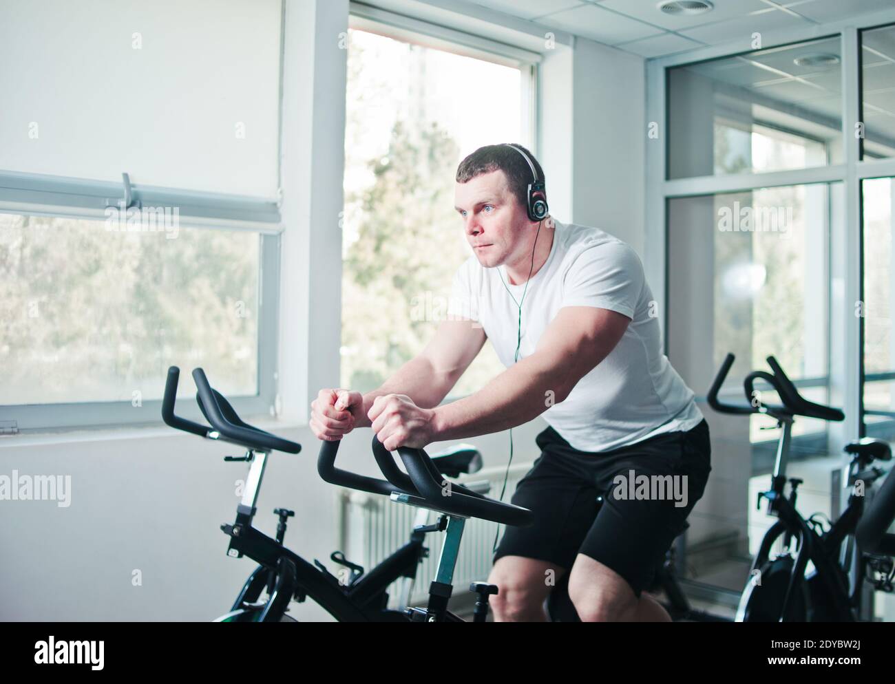 Concetto di stile di vita sano. Un giovane uomo sportivo in maglietta bianca e shorts si sta allenando in bicicletta alla classe di spinning . Allenamento cardio Foto Stock