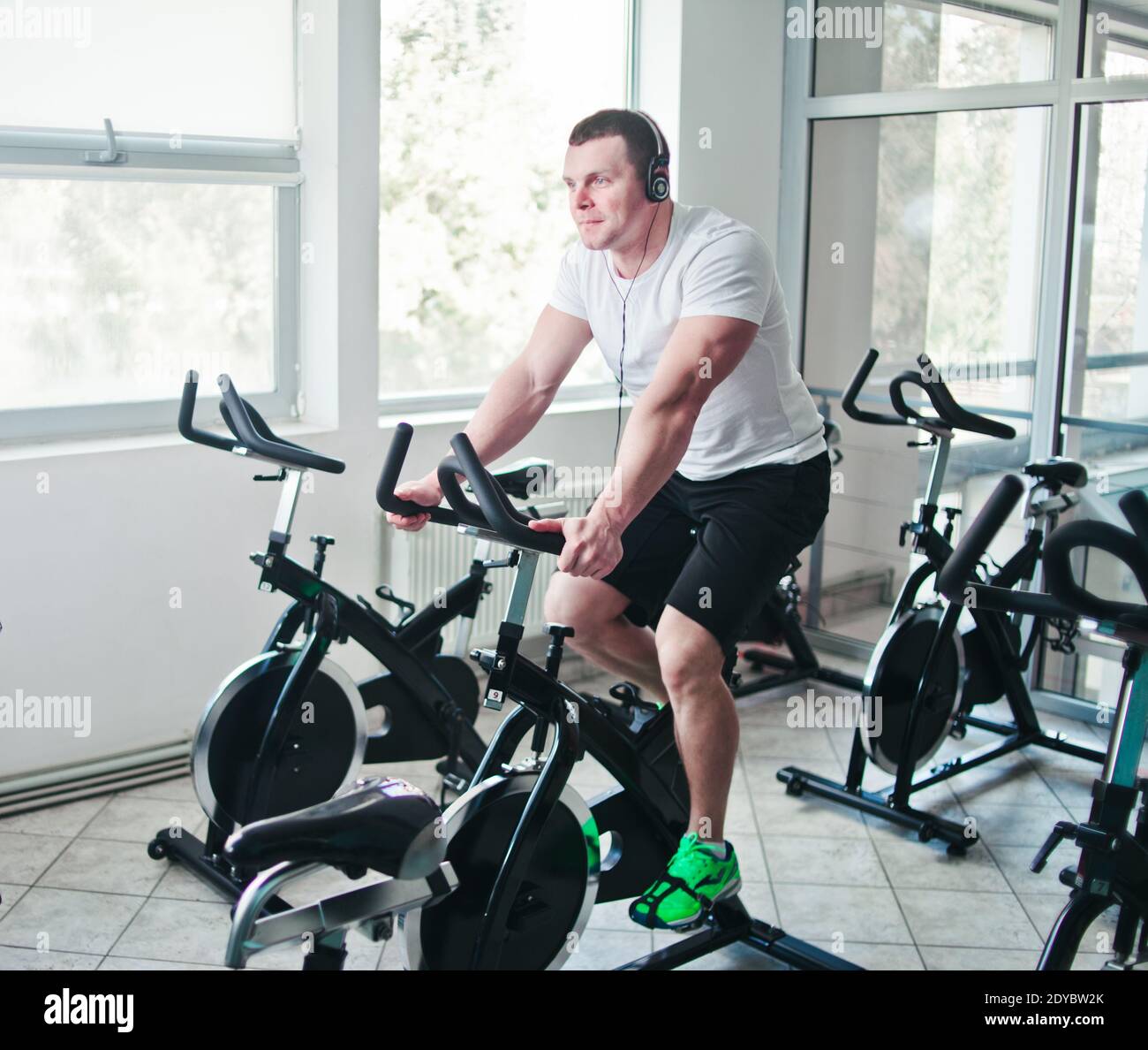 Concetto di stile di vita sano. Un giovane uomo sportivo in maglietta bianca e shorts si sta allenando in bicicletta alla classe di spinning . Allenamento cardio Foto Stock