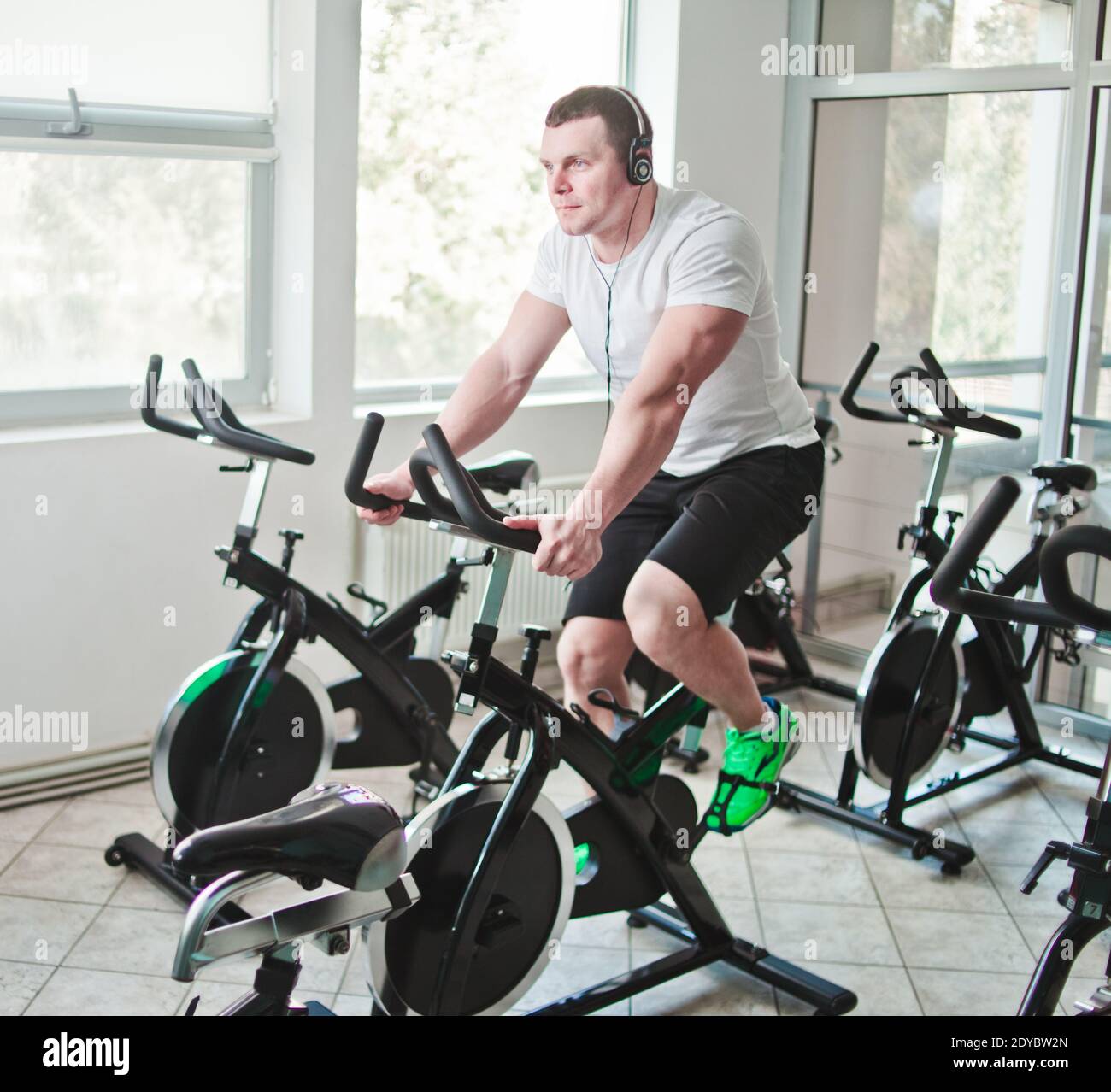 Concetto di stile di vita sano. Un giovane uomo sportivo in maglietta bianca e shorts si sta allenando in bicicletta alla classe di spinning . Allenamento cardio Foto Stock