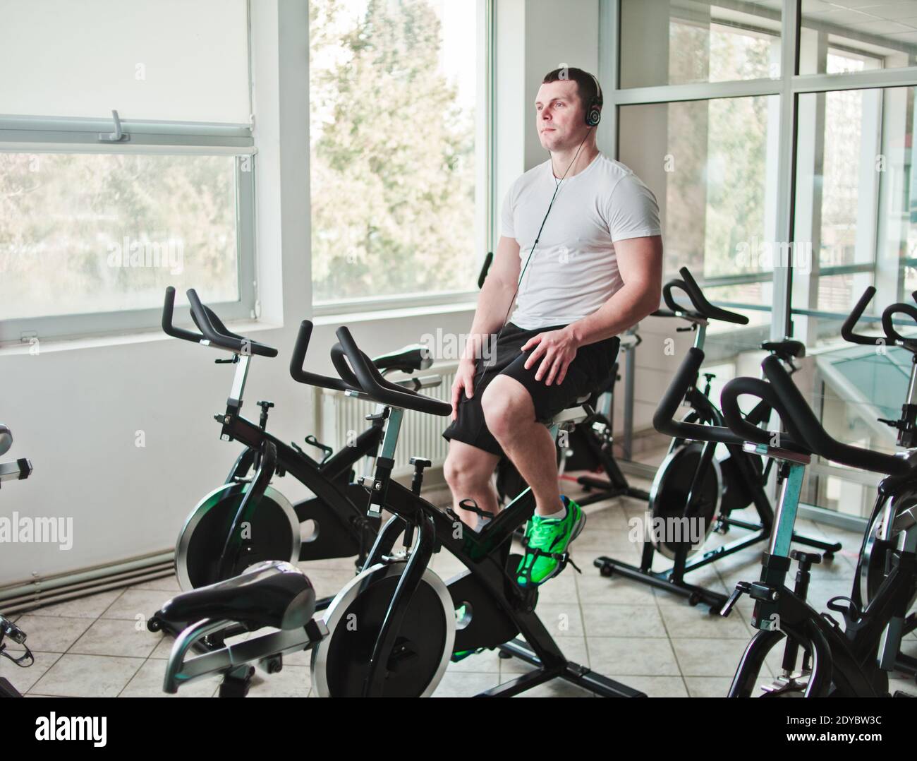 Concetto di stile di vita sano. Un giovane uomo sportivo con maglietta bianca e pantaloncini è in grado di allenarsi in bicicletta durante la lezione di spinning. Allenamento cardio Foto Stock