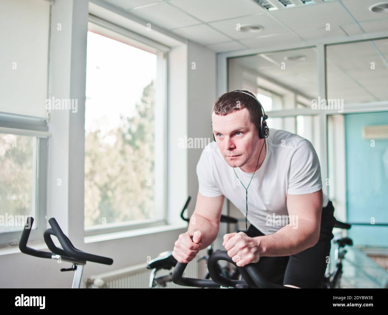 Concetto di stile di vita sano. Un giovane uomo sportivo in maglietta bianca e shorts si sta allenando in bicicletta alla classe di spinning . Allenamento cardio Foto Stock