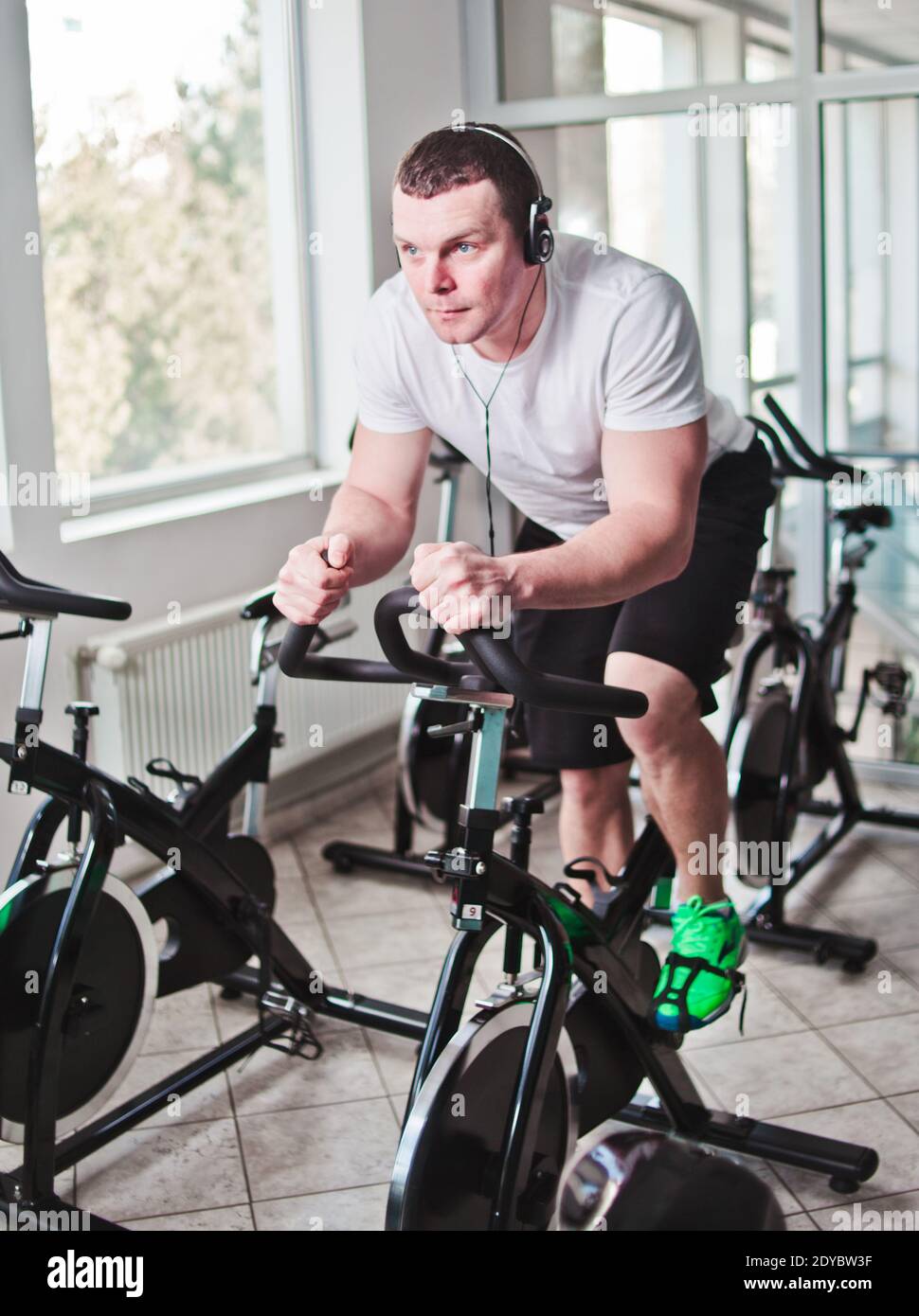 Concetto di stile di vita sano. Un giovane uomo sportivo in maglietta bianca e shorts si sta allenando in bicicletta alla classe di spinning . Allenamento cardio Foto Stock