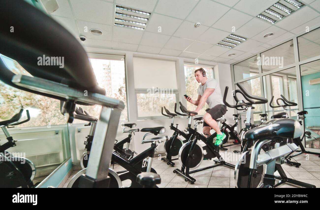 Concetto di stile di vita sano. Un giovane uomo sportivo in maglietta bianca e shorts si sta allenando in bicicletta alla classe di spinning . Allenamento cardio Foto Stock