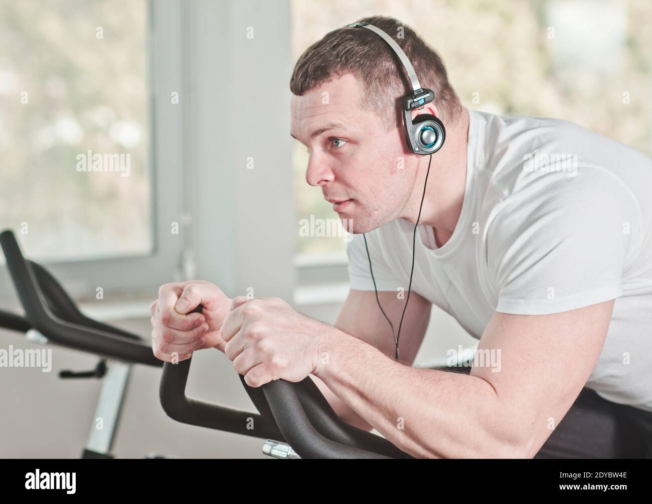 Concetto di stile di vita sano. Primo piano ritratto giovane uomo sportivo in t-shirt bianca e shorts si sta allenando in bicicletta in palestra per esercizi di gruppo. Cardio Foto Stock