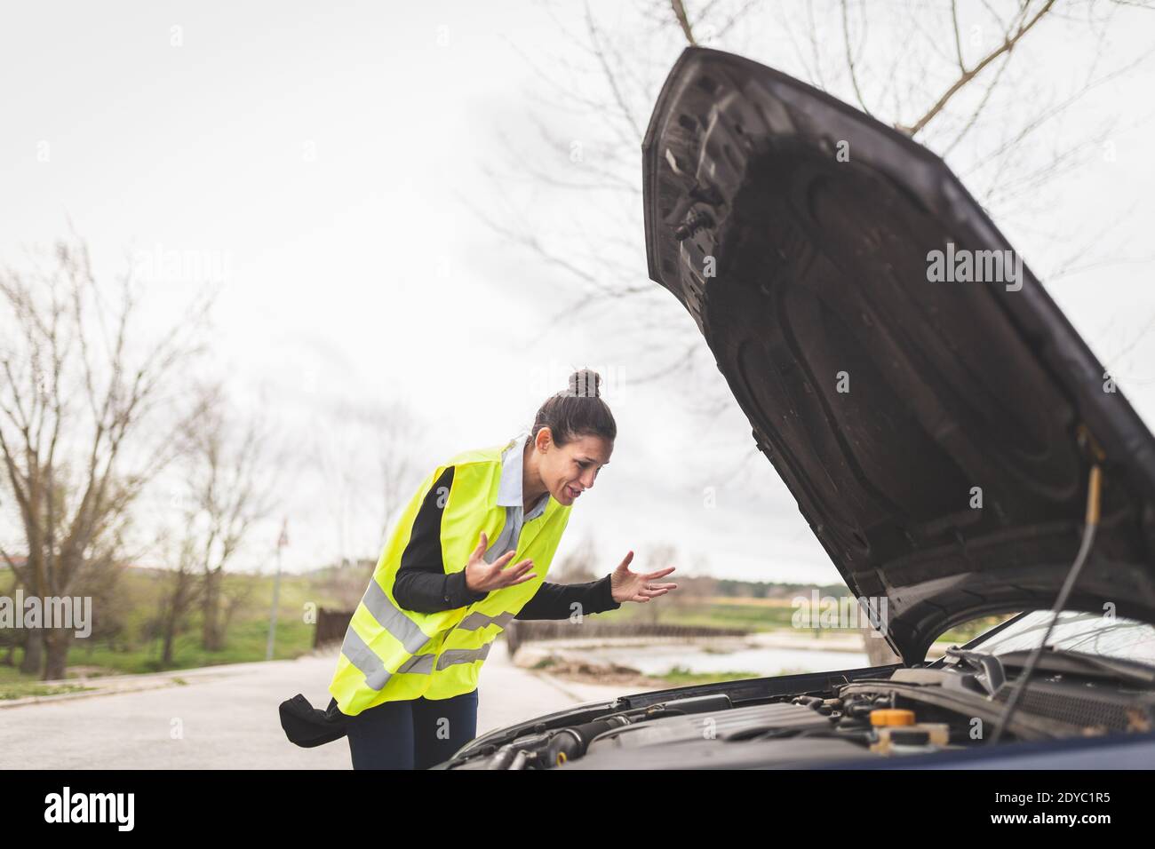 Giovane donna caucasica guardando il motore dell'automobile, non sa che cosa fare, l'automobile rotta giù nel mezzo della strada. Automobile e assistenza stradale Foto Stock