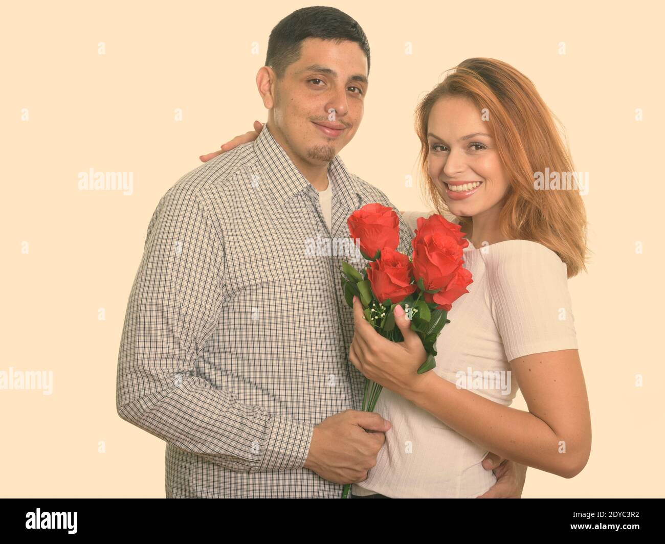 Giovane coppia felice sorridente e in amore tenendo rose rosse e abbracciando ogni altro Foto Stock