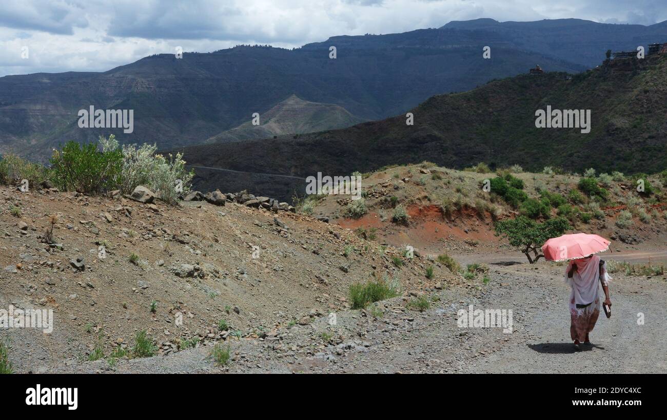 Lalibela-Etiopia: 12 aprile 2019: Donna con ombrello rosa che cammina sul sentiero sterrato al sole Foto Stock