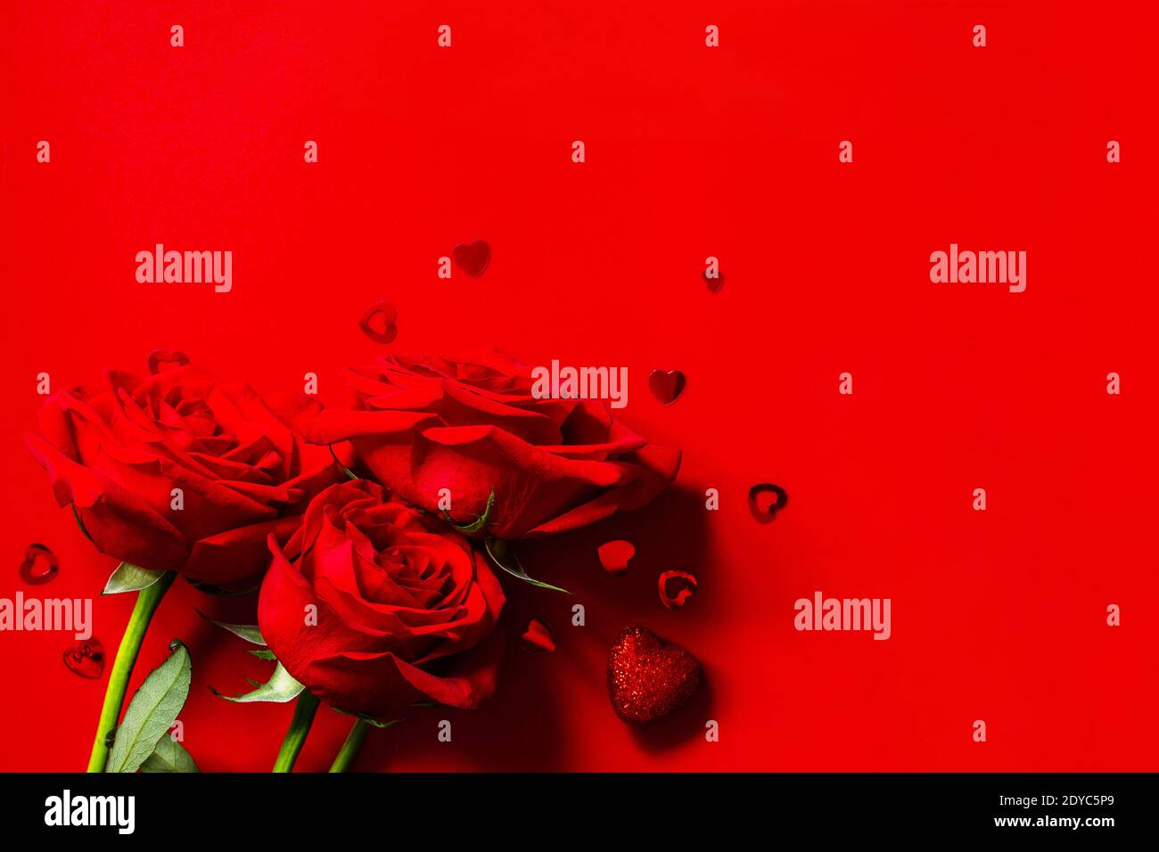 Rose rosse e decorazioni a forma di cuore su sfondo rosso. Spazio di copia per il vostro disegno o messaggio. Foto Stock