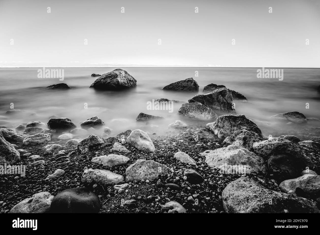 Foto in bianco e nero a lunga esposizione di rocce e onde vicino al mare Foto Stock