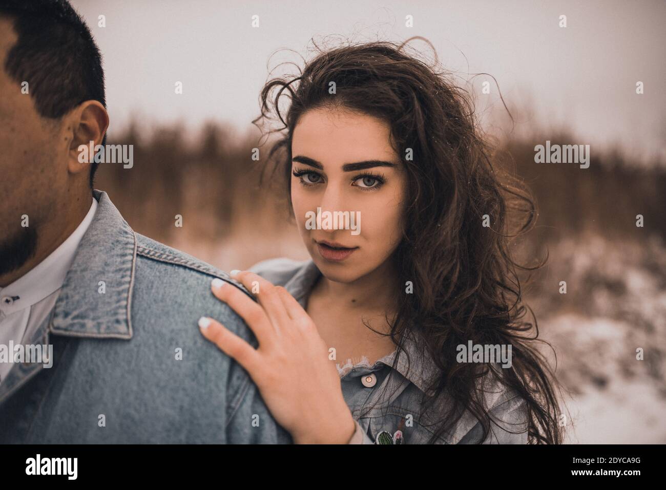 L'uomo ispanico messicano in denim giacca oversize e la donna sono baciante hugging ridere. Sposo e sposa matrimonio amore coppia in inverno nella neve. Moda Foto Stock