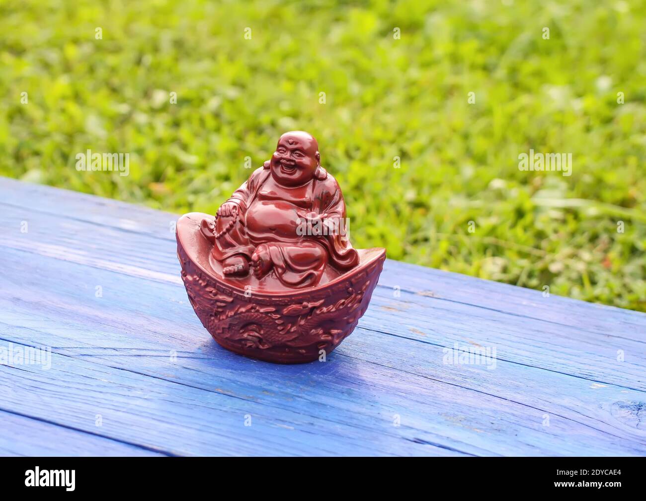 Statuina di buddha in ceramica su tavole di legno blu invecchiate nel parco estivo su sfondo verde erba . Foto Stock