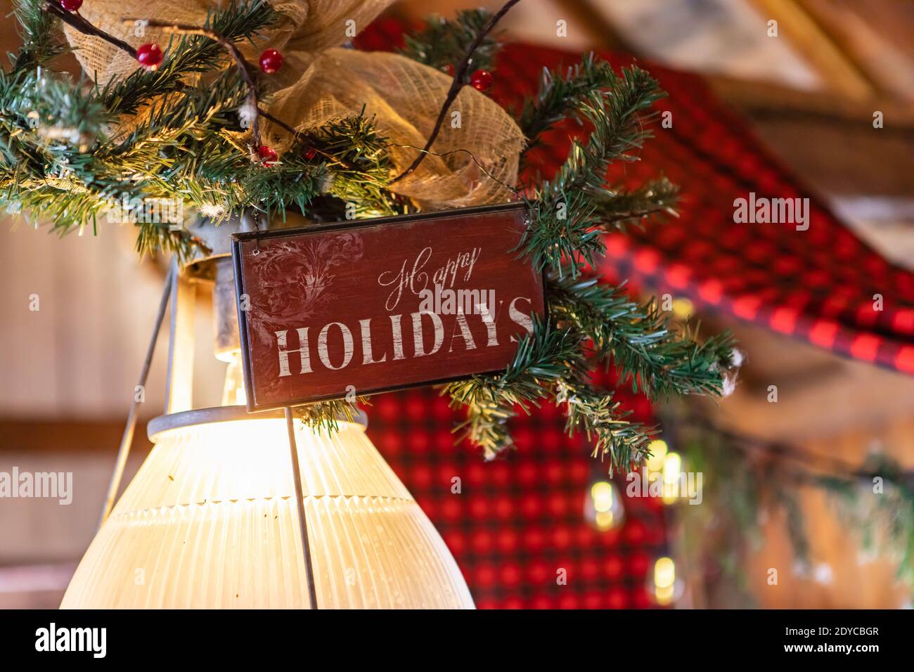 Fuoco selettivo di tavola di legno con testo scritto come felice vacanze decorate con decorazione di rami di abete e ornamenti di natale oltre la lampadina nel ristorante Foto Stock