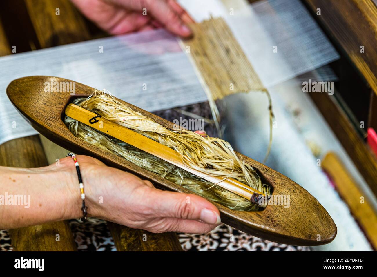 Una mano tiene la navetta di legno, carica di filato di fibra di kudzu, sopra il tessuto in corso di tessitura, in una bottega di tessitura nella regione di Hamamatsu, Giappone. Foto Stock
