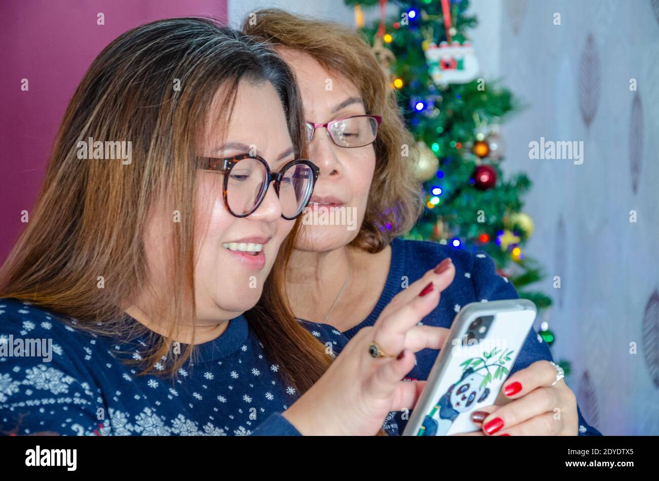 Una madre e la sua figlia cresciuta guardano insieme qualcosa su un telefono cellulare al tempo di Natale. Foto Stock