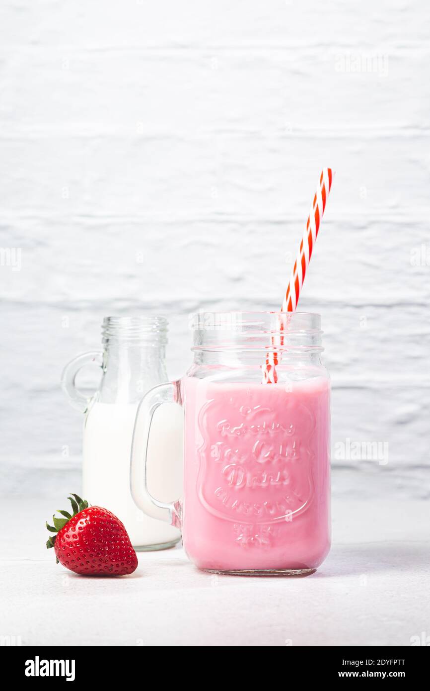 La fragola cade in un bicchiere da cocktail di latte creando schizzi su sfondo blu. Foto Stock