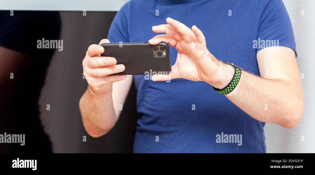 Anonimo giovane adulto, uomo che tiene l'iPhone 11 in mani scattando foto, closeup, Apple Watch al polso. Prodotti Apple stile di vita consumer, smartphone Foto Stock