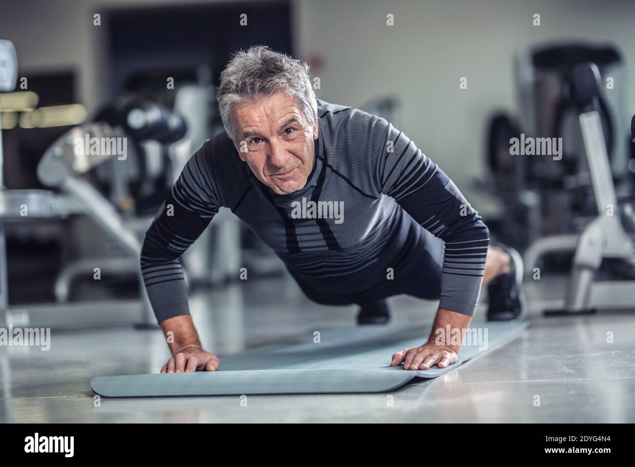 L'età è appena un numero ad un uomo con i capelli grigi che fanno i pushup in una palestra. Foto Stock