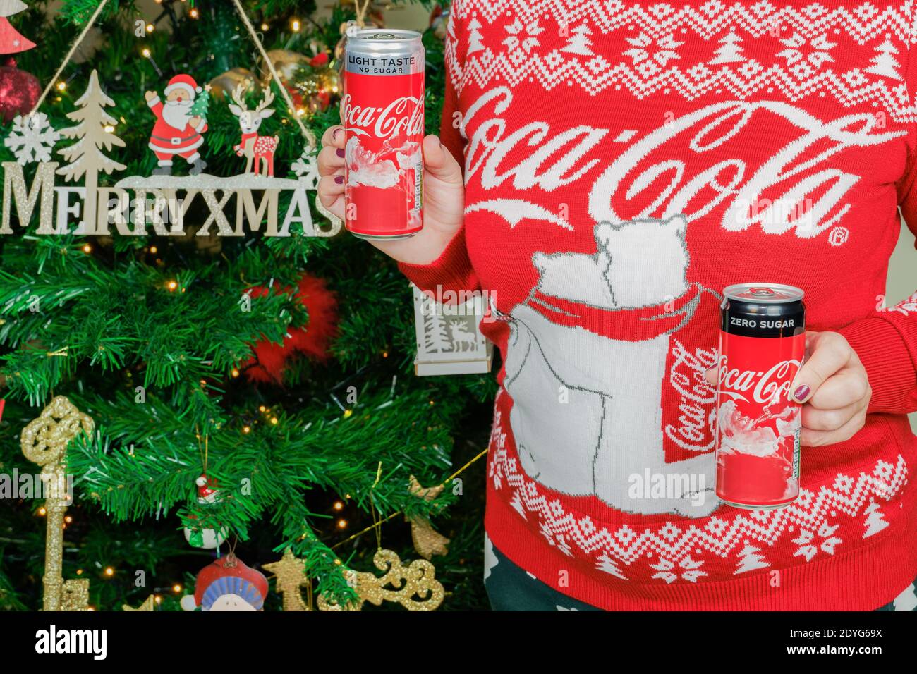 Femmina tiene Natale Coca Cola luce & zero lattine con Babbo Natale figura.Donna che indossa pullover con logo mostra bevande di stagione Prima dell'albero di Natale Foto Stock