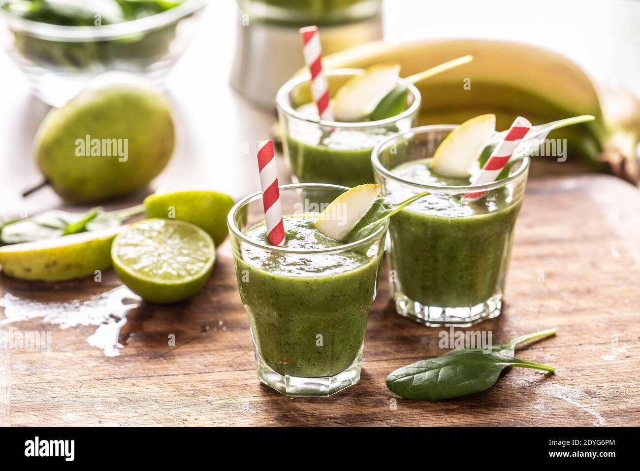 Tazze di frullato verde con cannucce di carta colorata e spicchi di lime su un tavolo. Foto Stock
