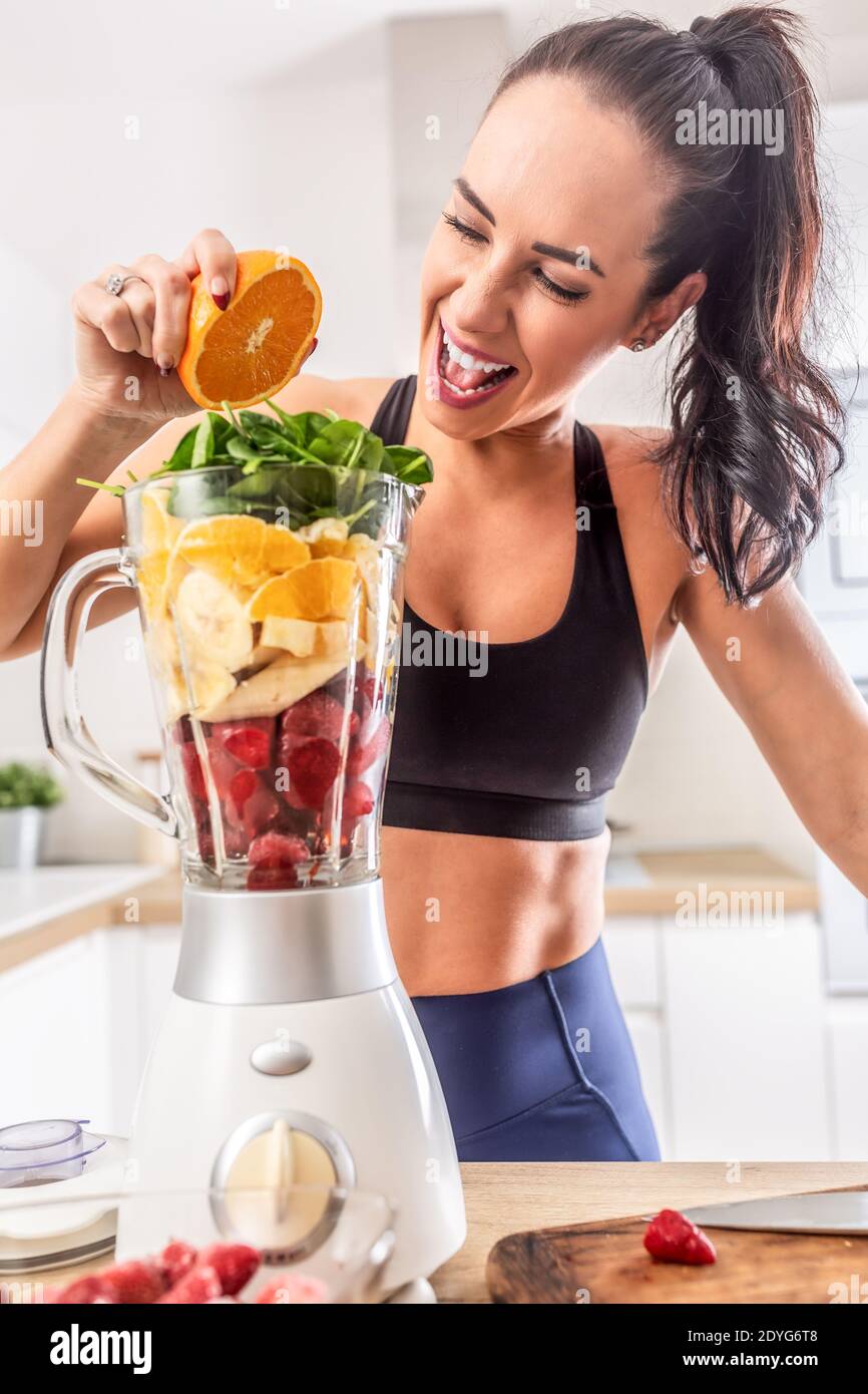 Fit ragazza spreme l'arancia in un mix colorato di frutta e verdura in un frullatore. Foto Stock Fit ragazza spreme l'arancia in un mix colorato di frutta e verdura in un frullatore. Foto Stock