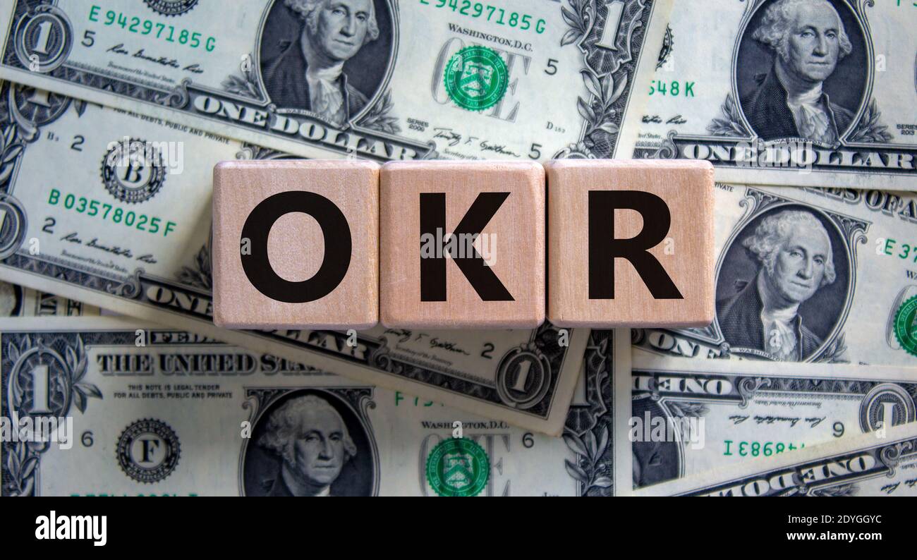 Simbolo OKR. Parole di concetto 'OKR - obiettivi e risultati chiave' su cubi di legno su uno sfondo bello dalle fatture del dollaro. Business e OKR - obiettivo Foto Stock