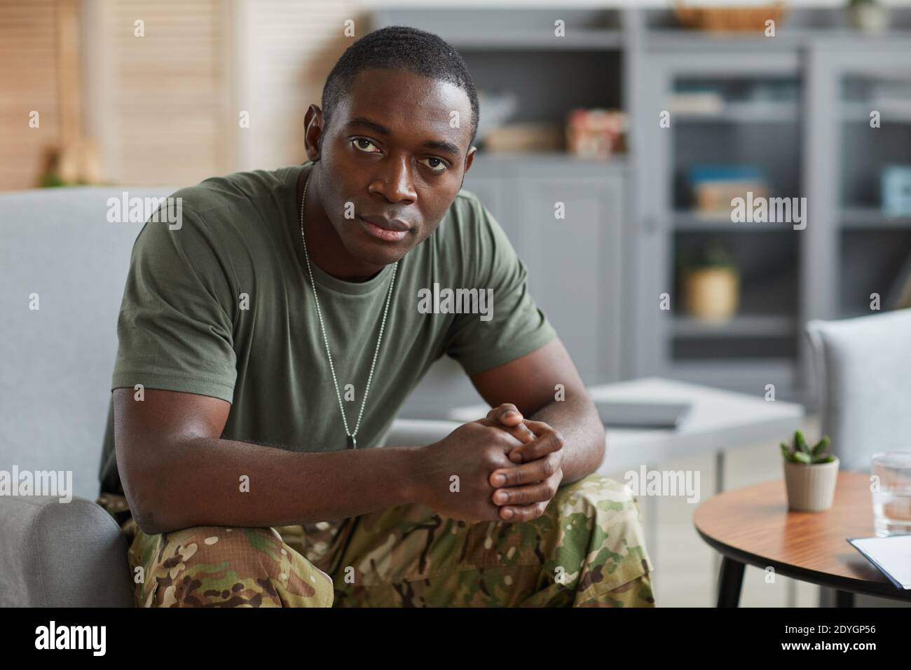 Ritratto di un militare africano che guarda la macchina fotografica mentre è seduto sul divano a casa Foto Stock