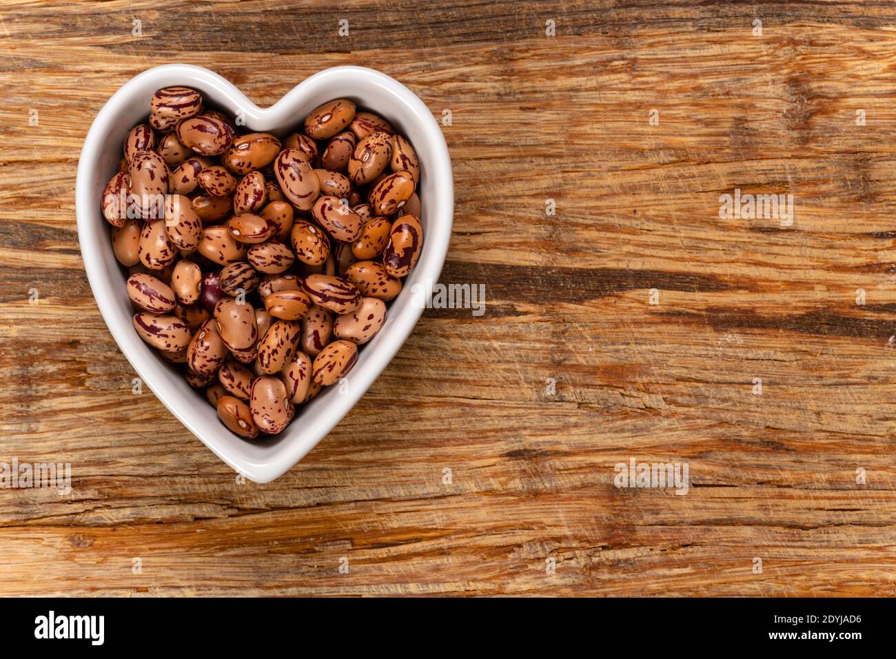 Fagioli bianchi di cargamanto, conosciuti anche come mirtilli rossi, borlotti o fagioli Romani in una ciotola a forma di cuore. Vista dall'alto. Foto Stock