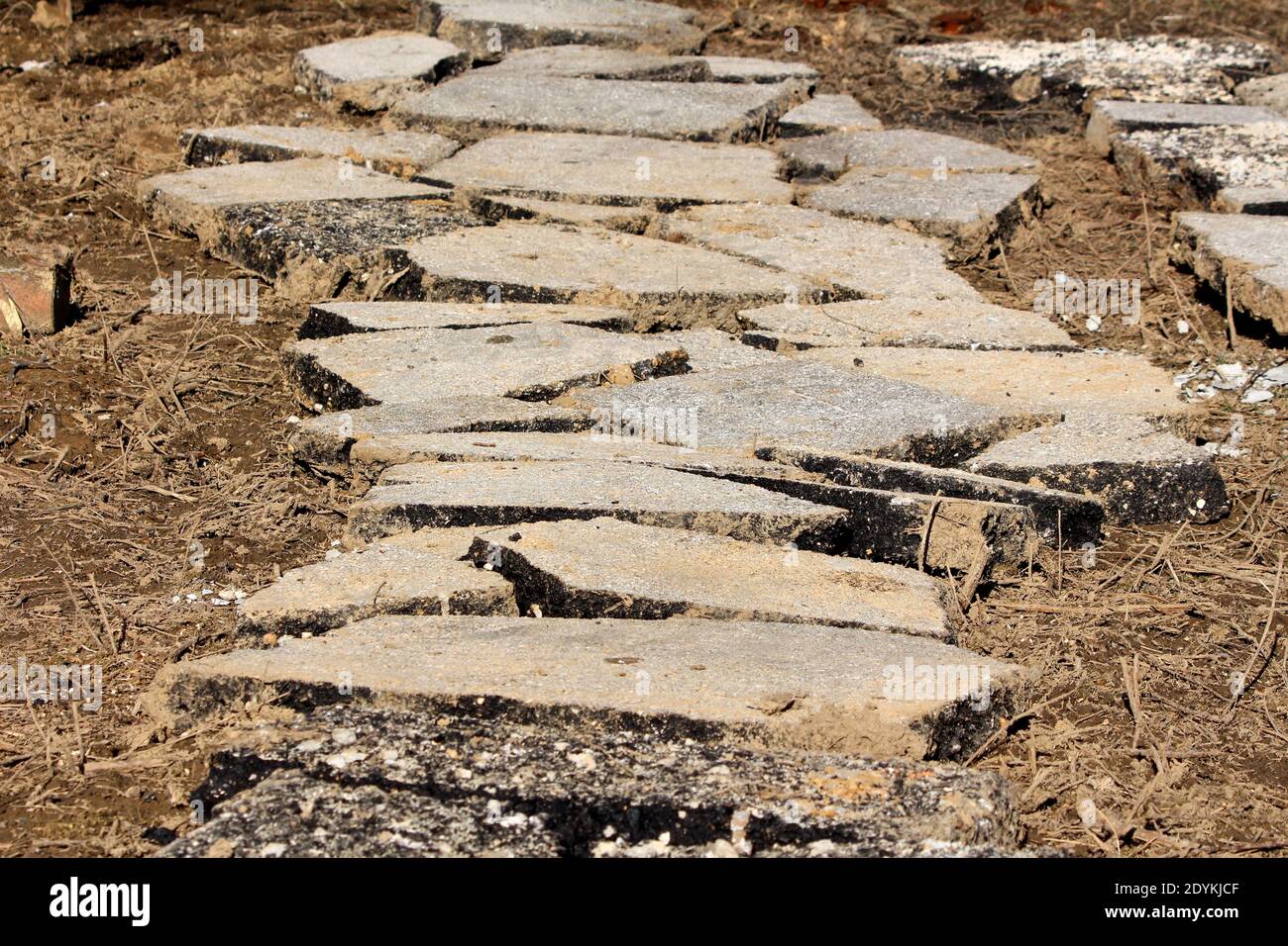 Lastre rotte incrinate da asfalto asfaltato distrutto impilato insieme formare un percorso su suolo bagnato mescolato con asciutto erba su freddo sole giornata invernale Foto Stock