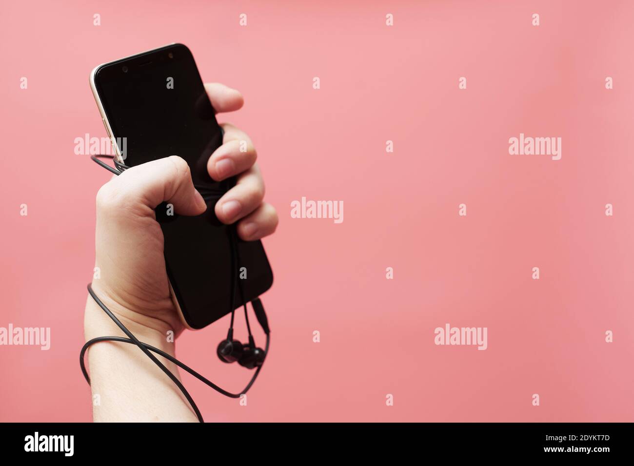 Concetto di dipendenza musicale, smartphone legato a mano con filo su sfondo rosa Foto Stock