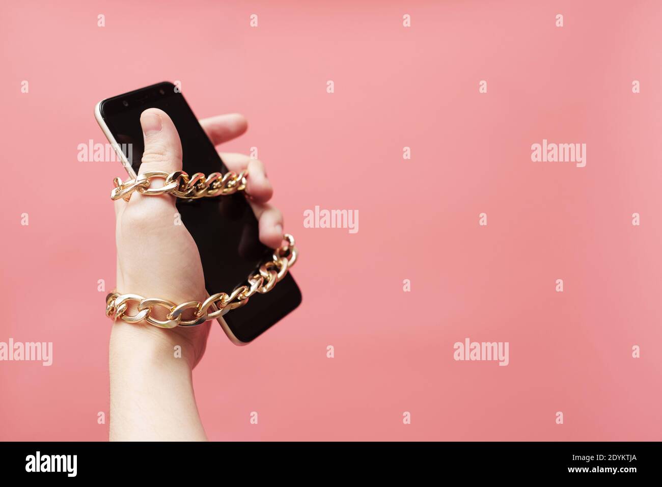 Dipendenza dal telefono, concetto di social network, legato a mano con uno smartphone a catena su sfondo rosa Foto Stock