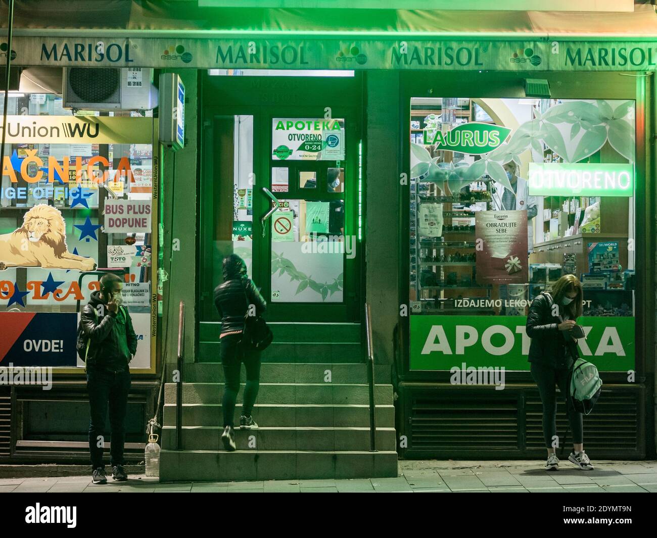 BELGRADO, SERBIA - 10 NOVEMBRE 2020: Giovani, ragazze e ragazzi, in piedi e in attesa di notte di fronte ad una farmacia indossare maschera protettiva eq Foto Stock