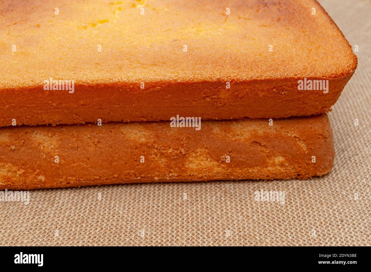 Torta di spugna fatta in casa, in portoghese Pão De lo. Cima della pasta per torte cotta al forno. Isolato su sfondo juto. Vista frontale. Foto Stock