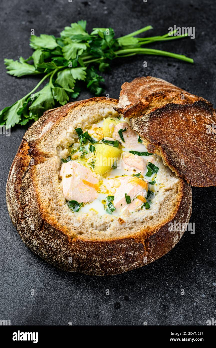 Zuppa finlandese di pesce cremoso con salmone, trota, patate servite nel pane. Sfondo nero, vista dall'alto. Foto Stock