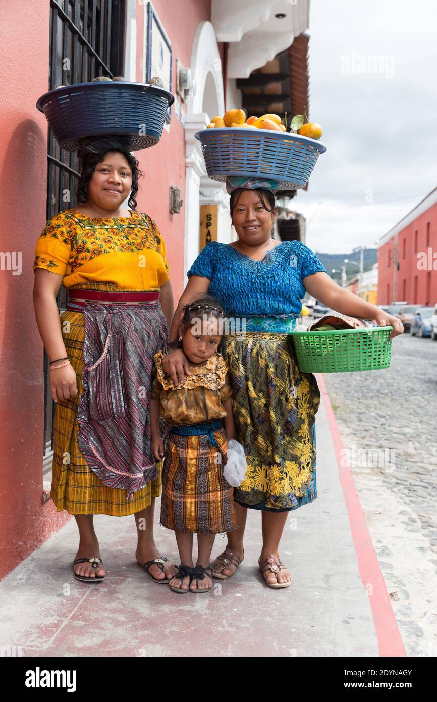 Antigua, Guatemala le donne che trasportano cestini di frutta sulle loro teste posano con la ragazza Foto Stock