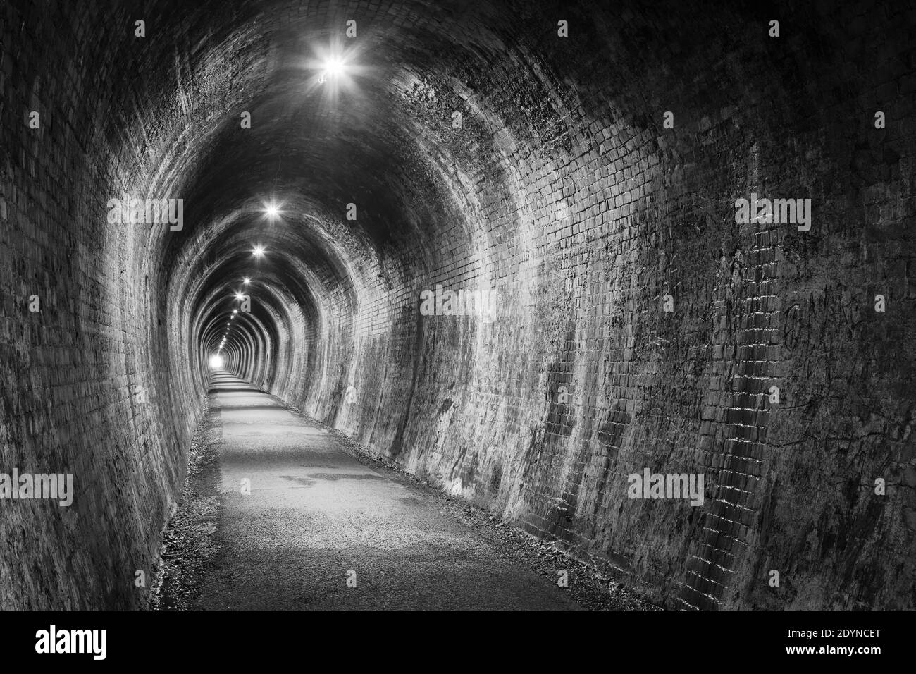 Un vecchio tunnel di mattoni, illuminato con illuminazione elettrica. Bianco e nero. Fotografato nell'ex tunnel ferroviario di Karangahake Gorge, Nuova Zelanda Foto Stock
