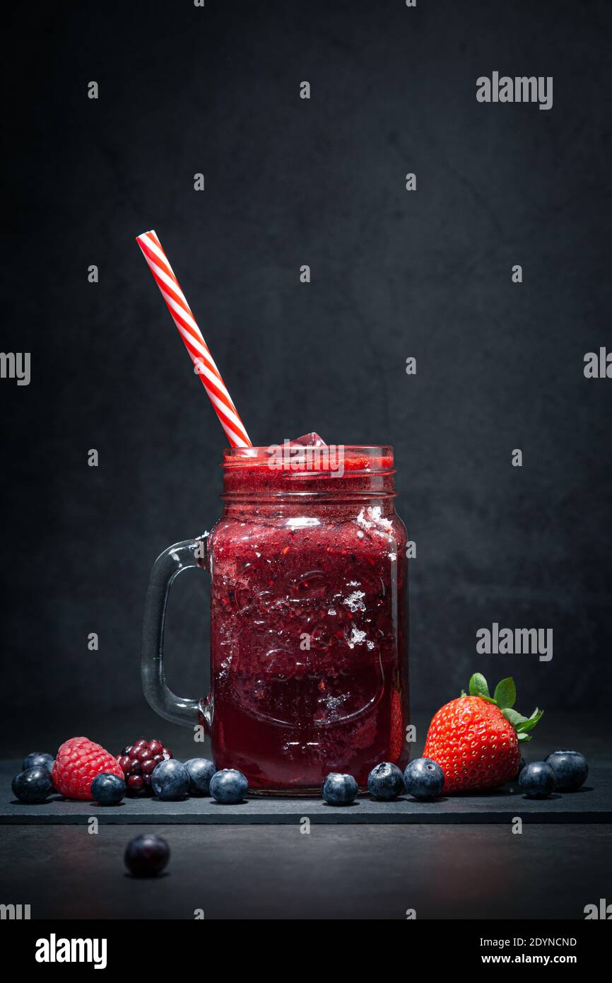 Bacche Smoothie in vaso di vetro con paglia e bacche assortite su sfondo scuro. Foto Stock