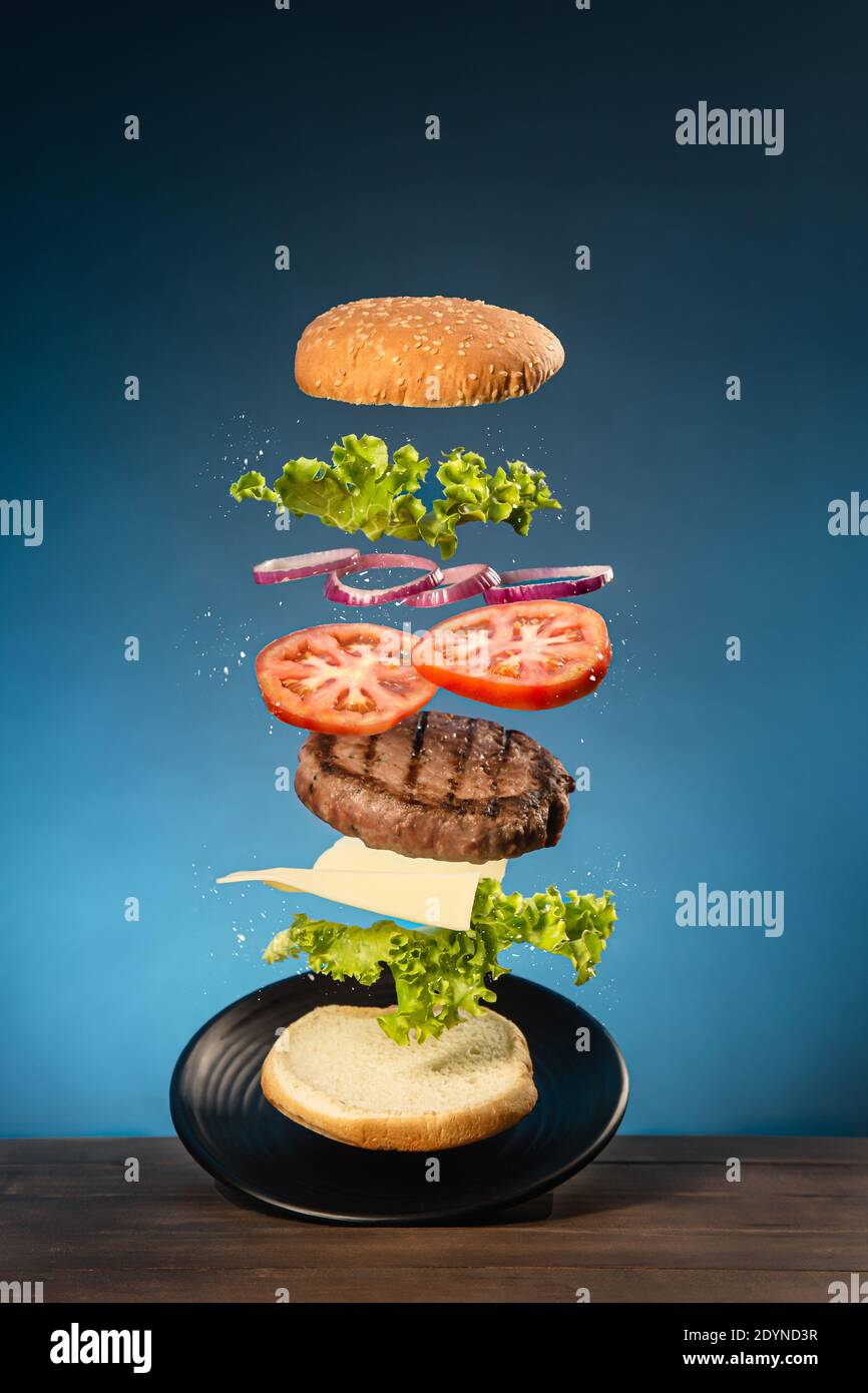 Hamburger volanti su base di legno e sfondo blu. Foto Stock