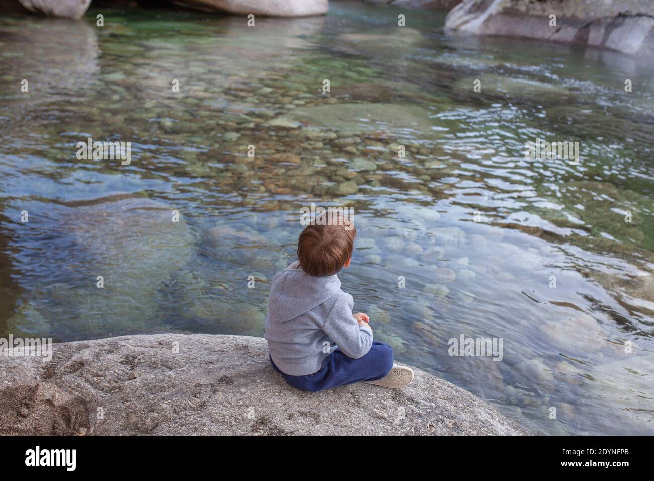 Piccolo ragazzo seduto in riva al fiume di montagna. Godere della natura per bambini concetto Foto Stock