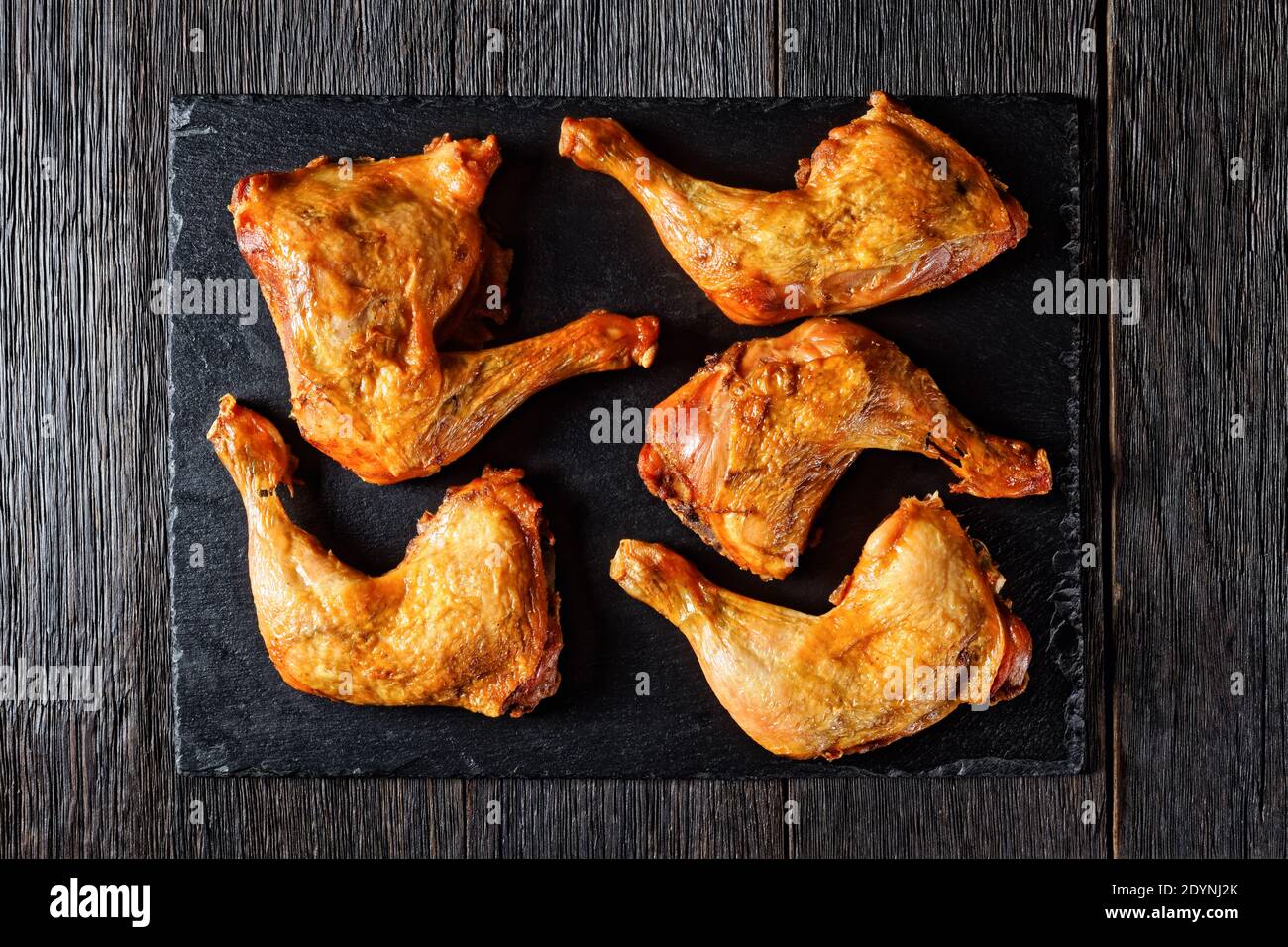 cosce di pollo arrosto croccanti servite su un vassoio di ardesia nera su un tavolo di legno scuro, vista orizzontale dall'alto Foto Stock