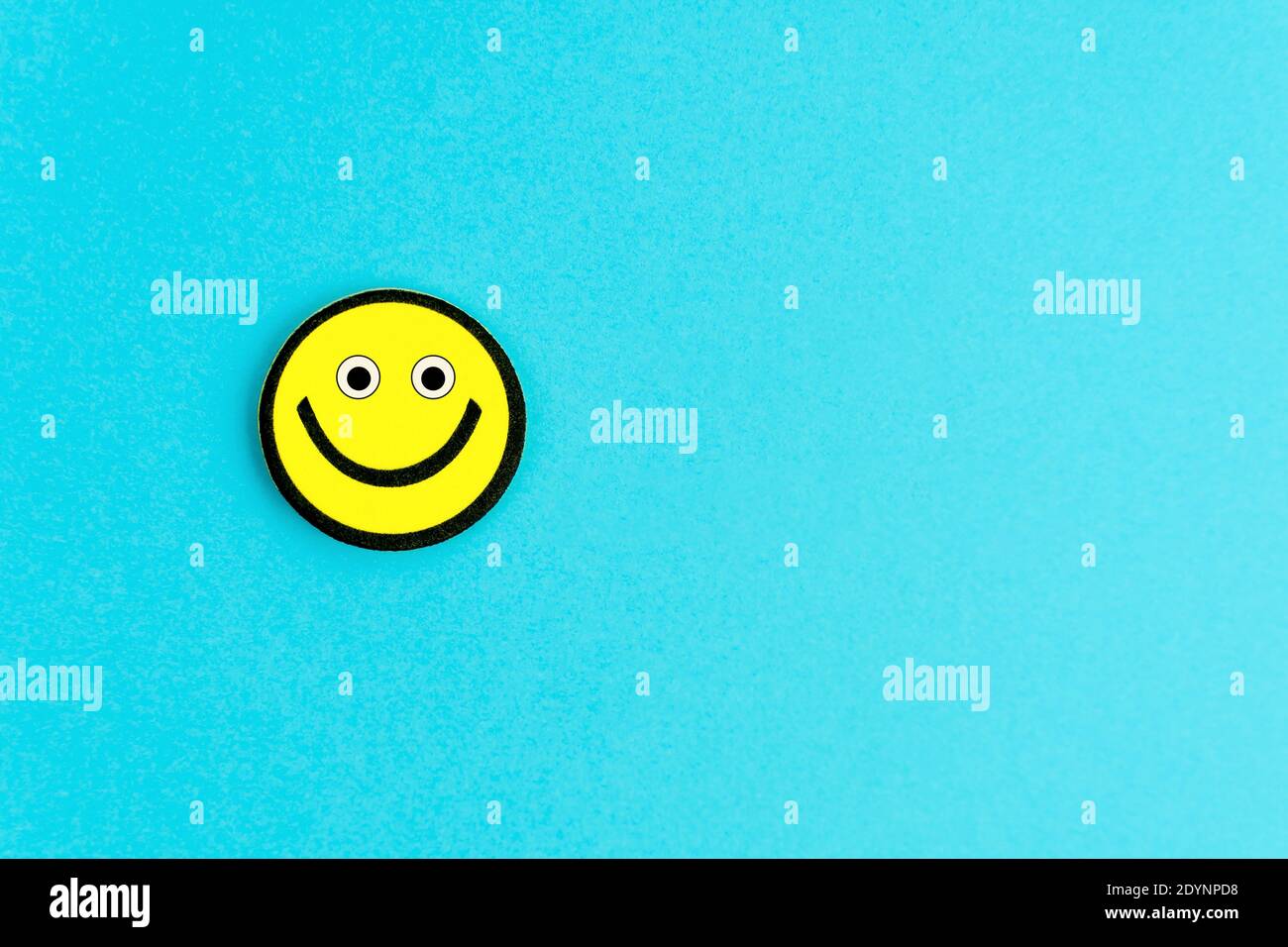Emoticon gialla con occhi divertenti su sfondo blu luminoso. Auguri di buon giorno. Copiare spazio per il testo Foto Stock