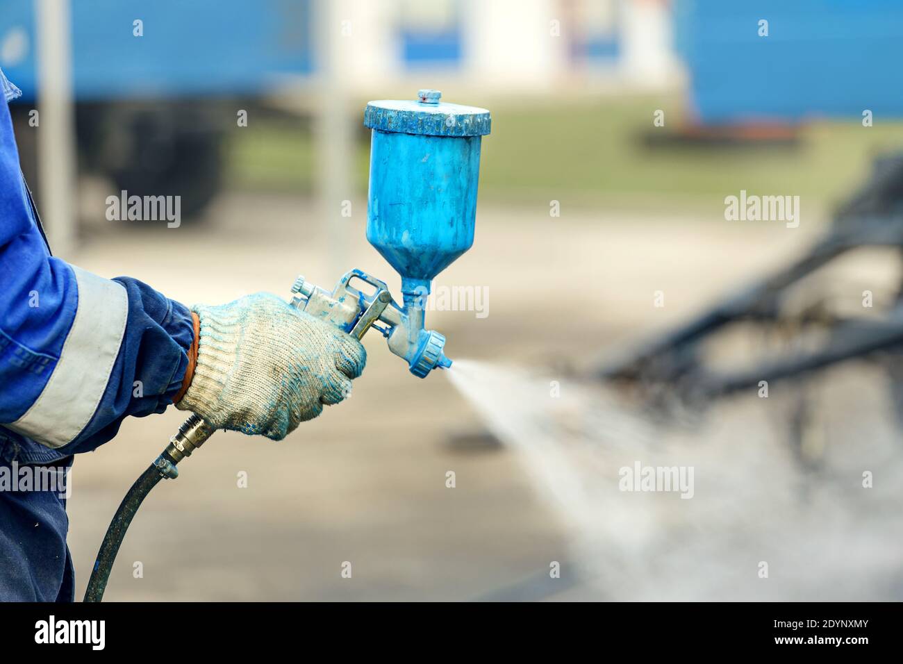 Pistola a spruzzo in mano. Un lavoratore in tute e un guanto tiene in mano un compressore spray per la verniciatura. Foto Stock