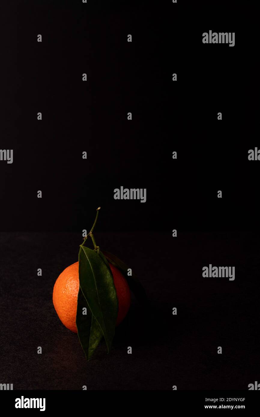 Un tangerino con foglie sul tavolo nel buio, moody Foto Stock